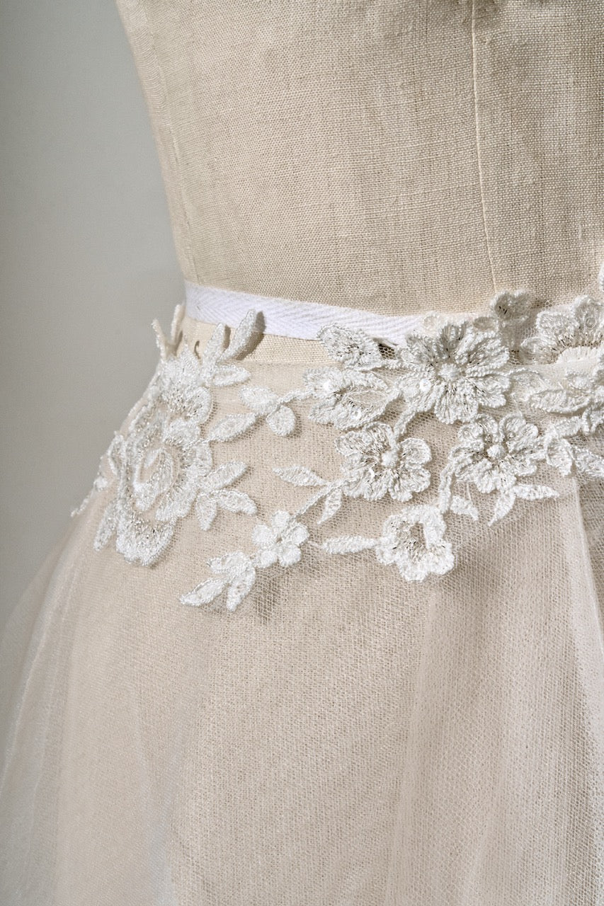 Close-up of a beige dress with lace detailing on a plain background