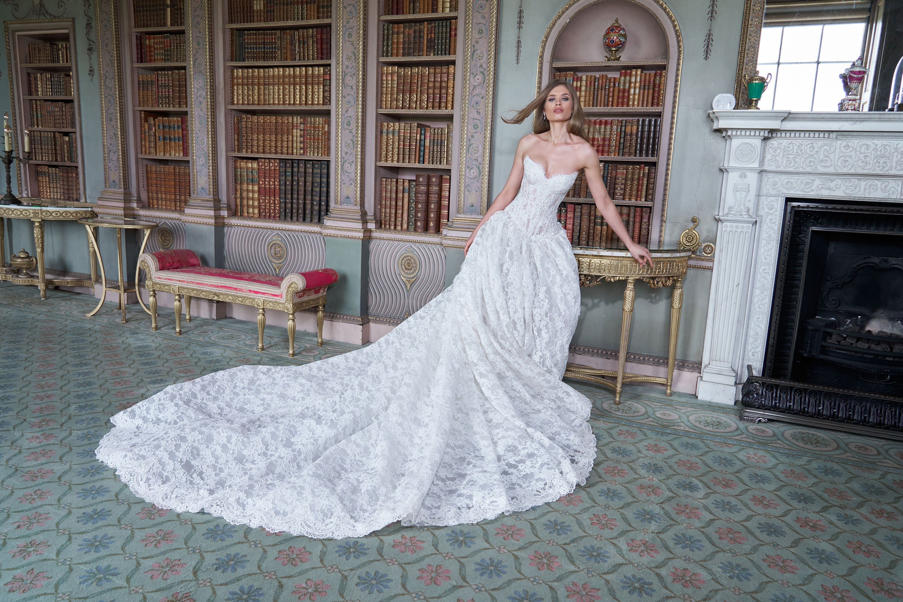 Woman in a white wedding dress standing in a grand room with bookshelves and a fireplace.