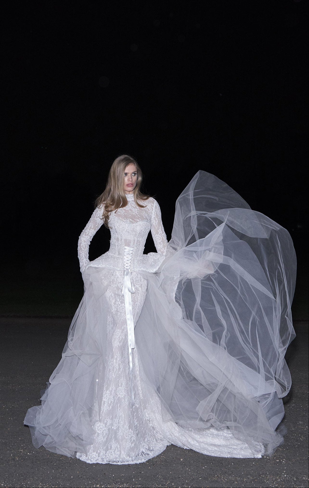 Model wearing a white wedding dress with a long train against a black background
