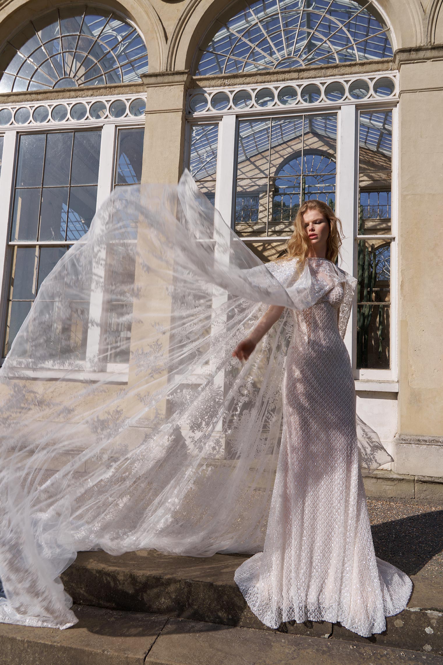 Woman in a white lace dress standing in front of large glass windows