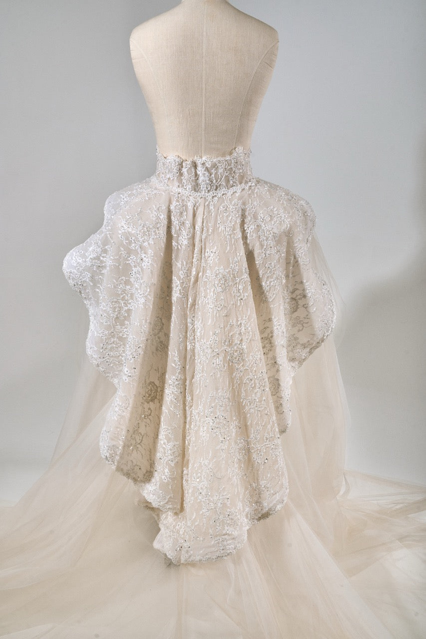 White lace wedding dress on a mannequin against a plain background
