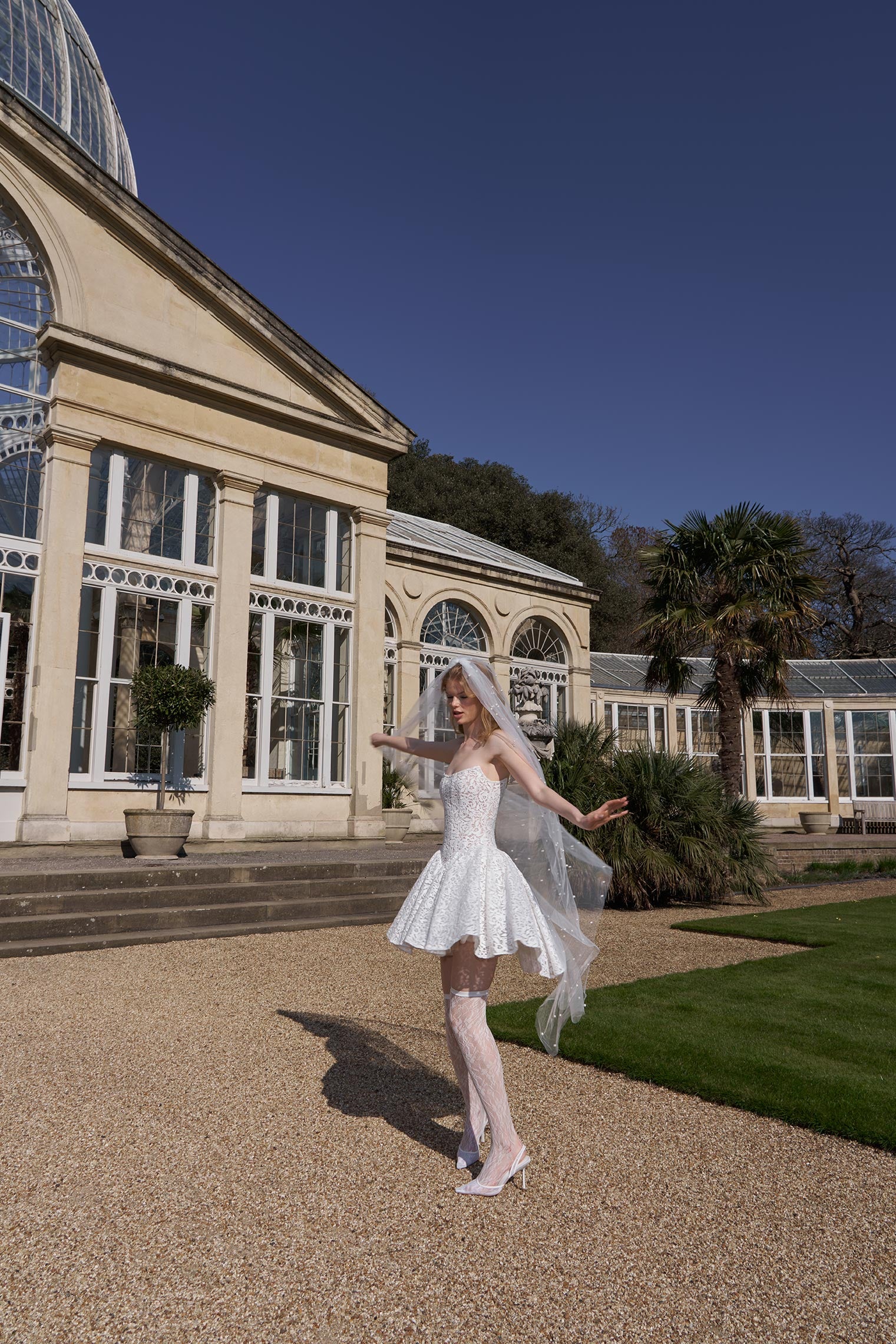 Bride in a white wedding dress standing in front of a conservatory building.