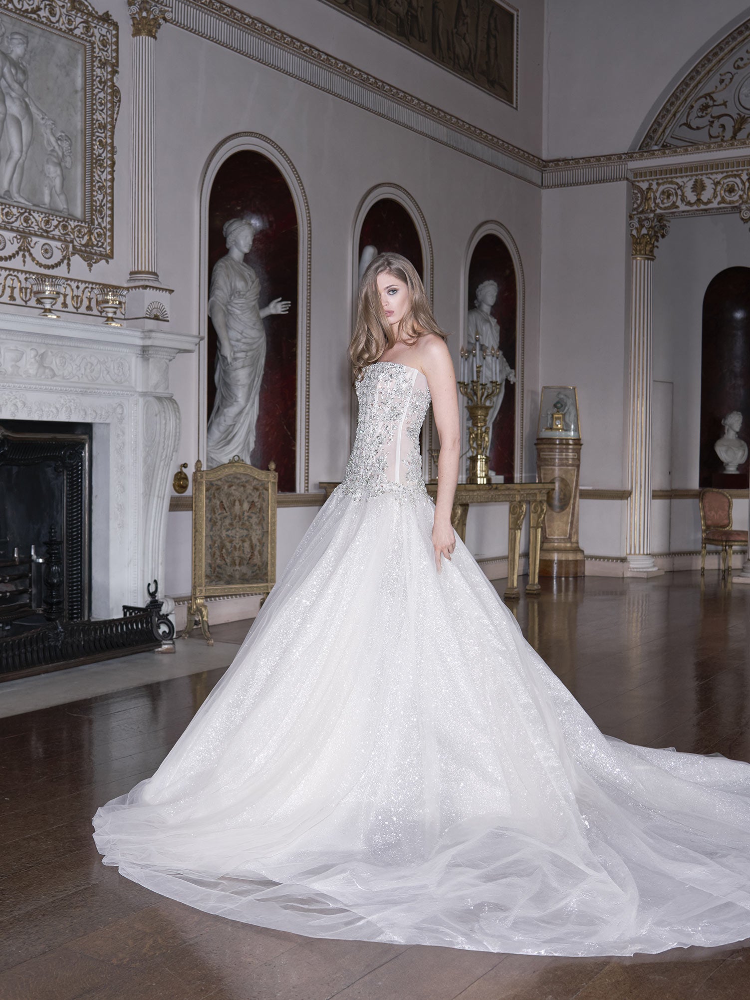 Woman in a white wedding dress standing in an elegant room with classical decor.