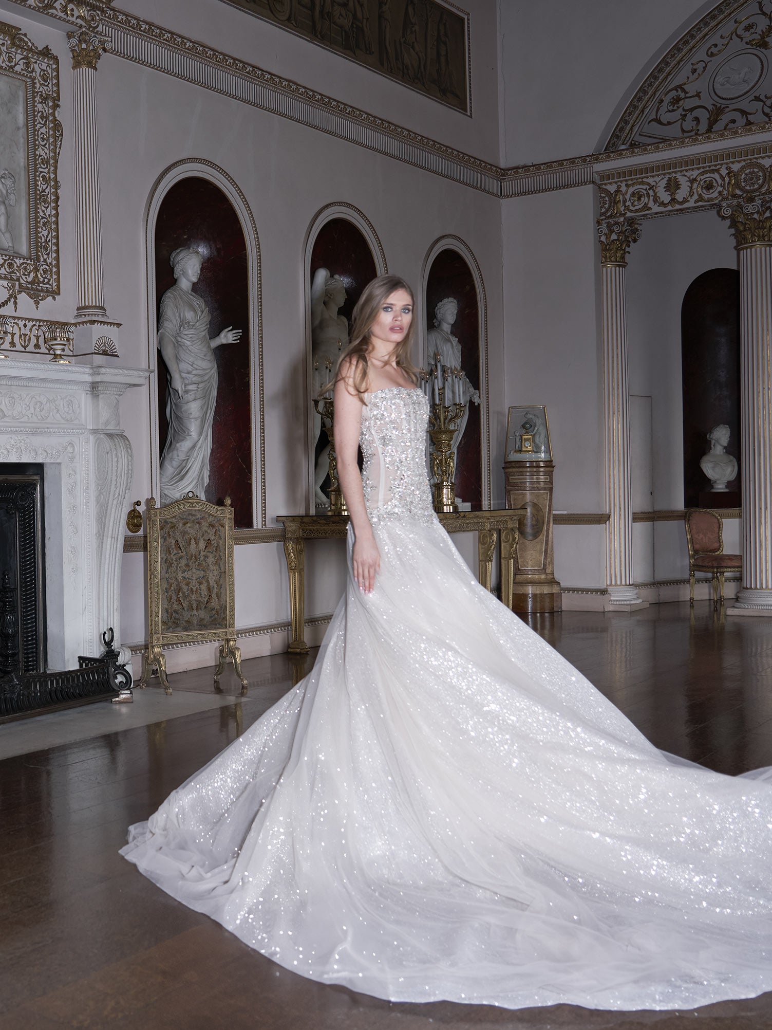Woman in a white wedding dress standing in an elegant room with statues and decorative elements.