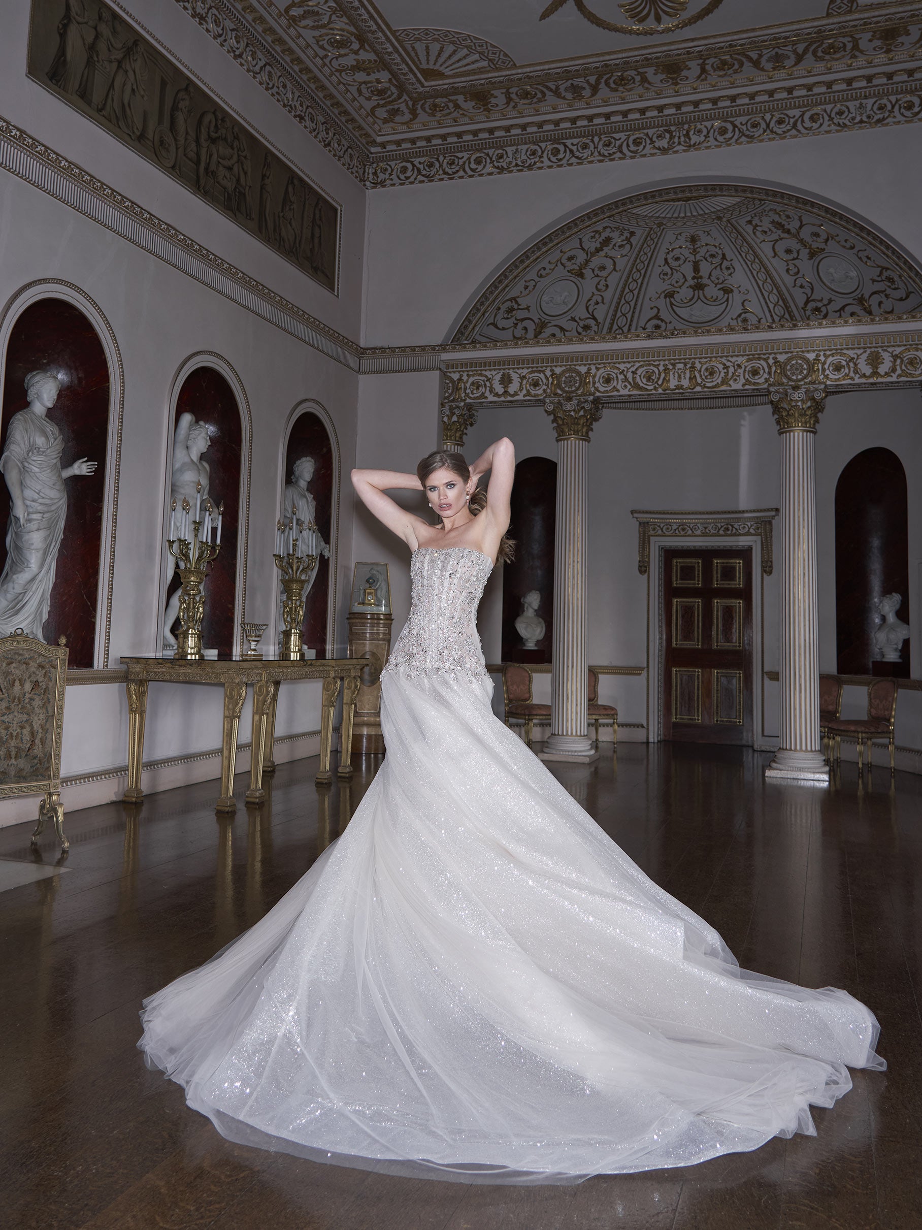 Woman in a white wedding dress standing in an elegant room with statues and decorative columns.