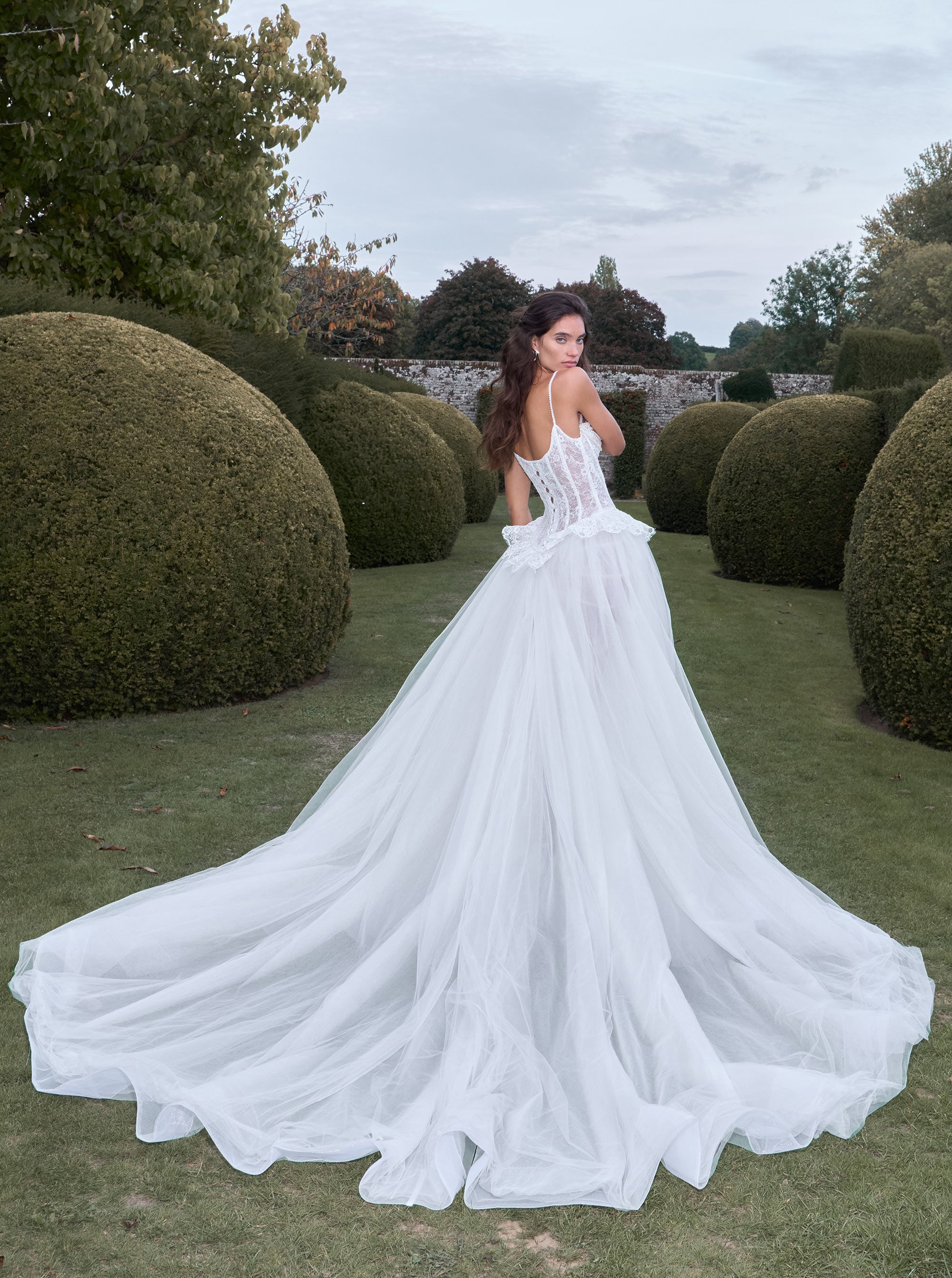 Woman in a white wedding dress standing in a garden with manicured hedges.