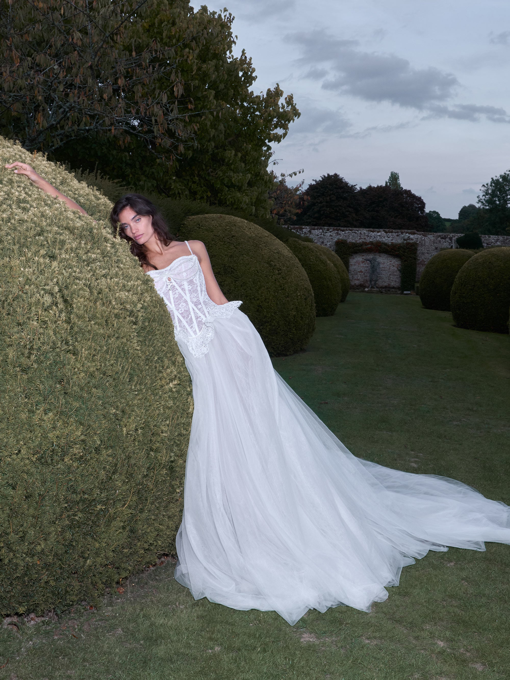 Woman in a white dress standing in a garden with large spherical bushes.
