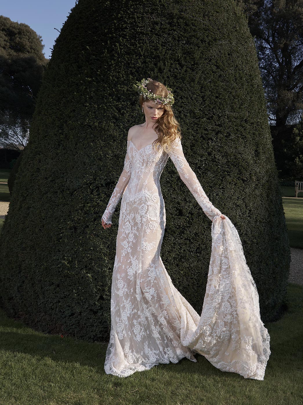 Woman in a lace wedding dress standing outdoors with trees in the background