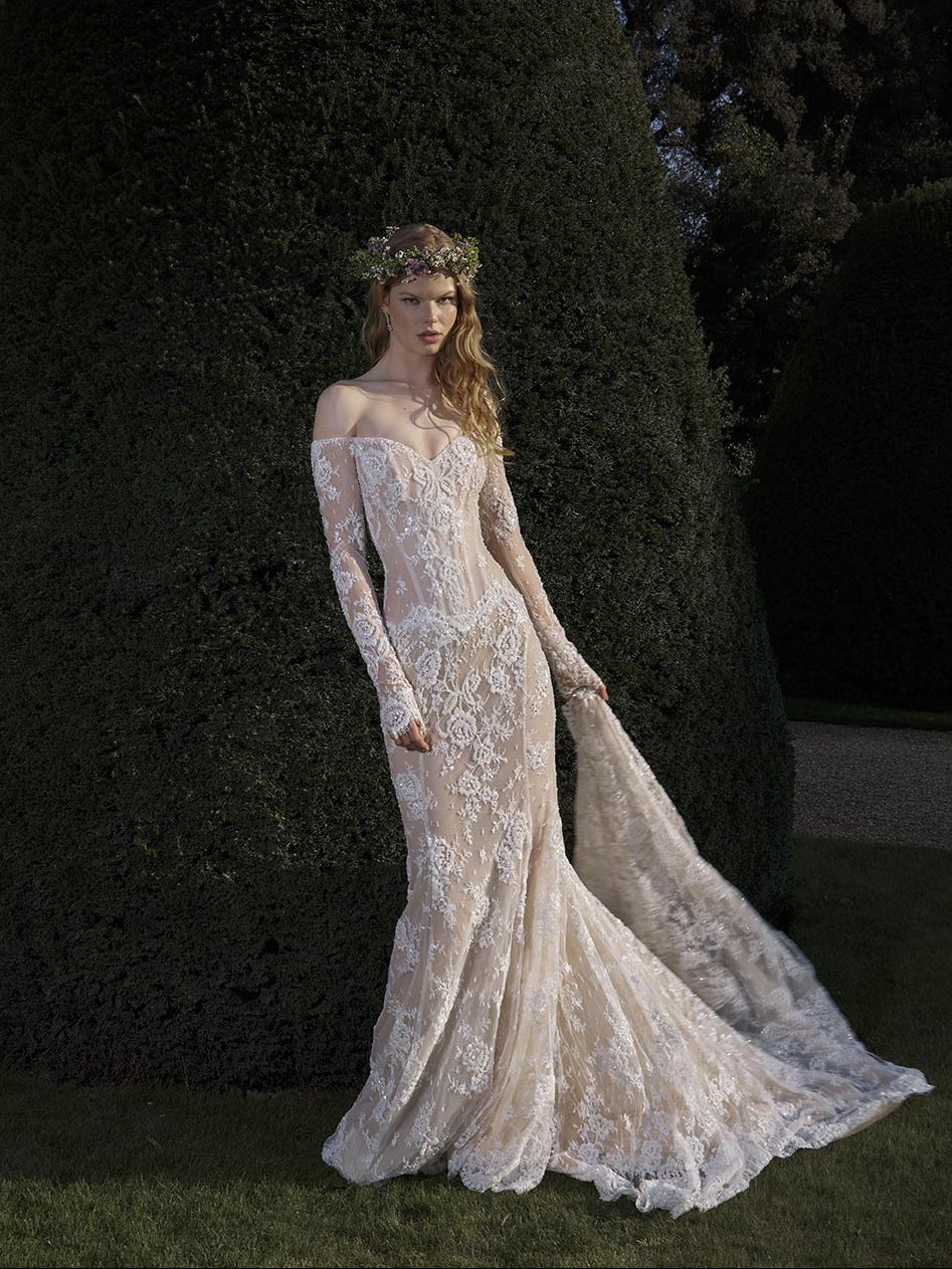 Woman in a lace wedding dress standing outdoors with trees in the background