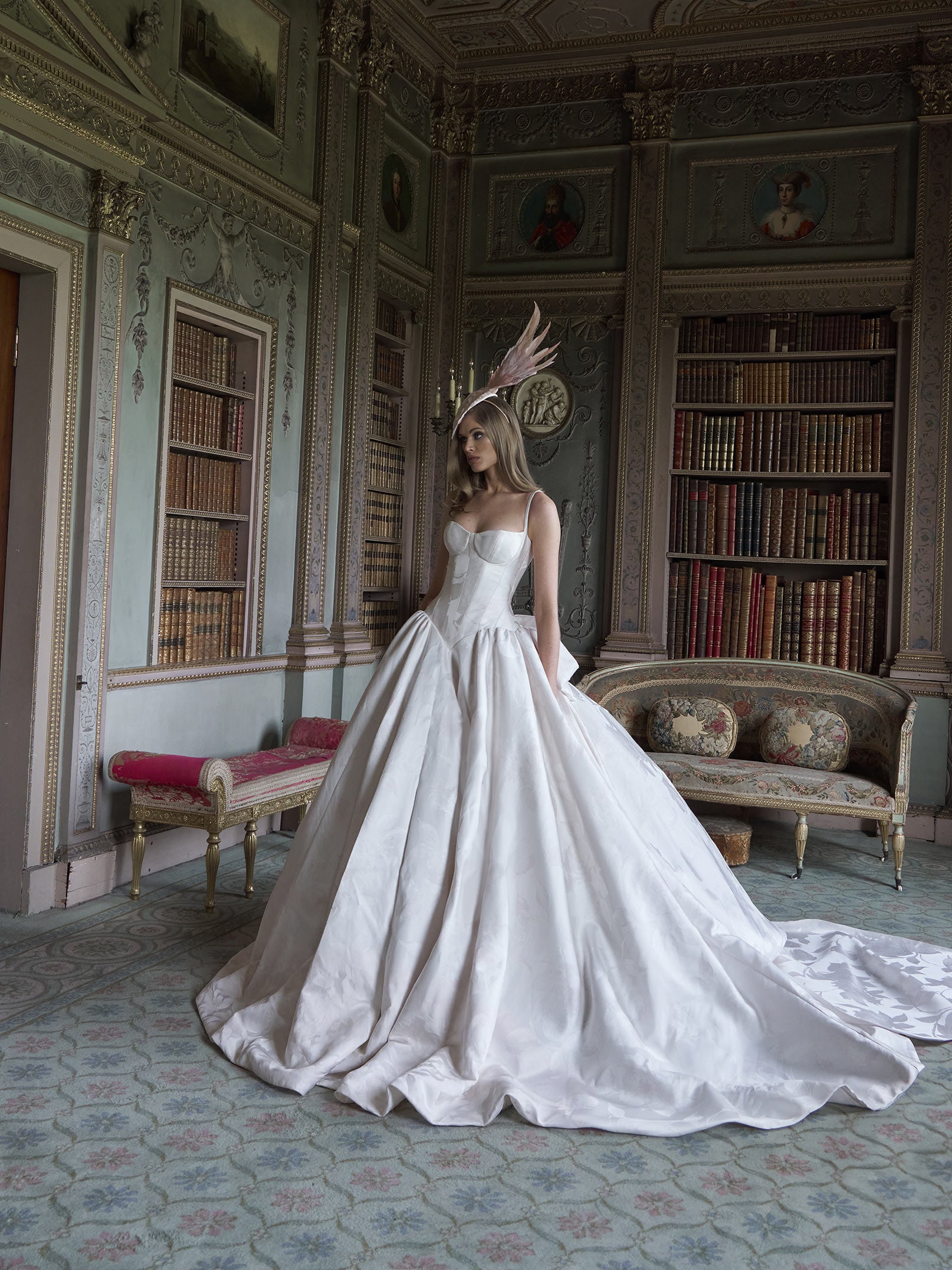 Woman in a white wedding dress standing in an ornate room with bookshelves and decorative furniture.