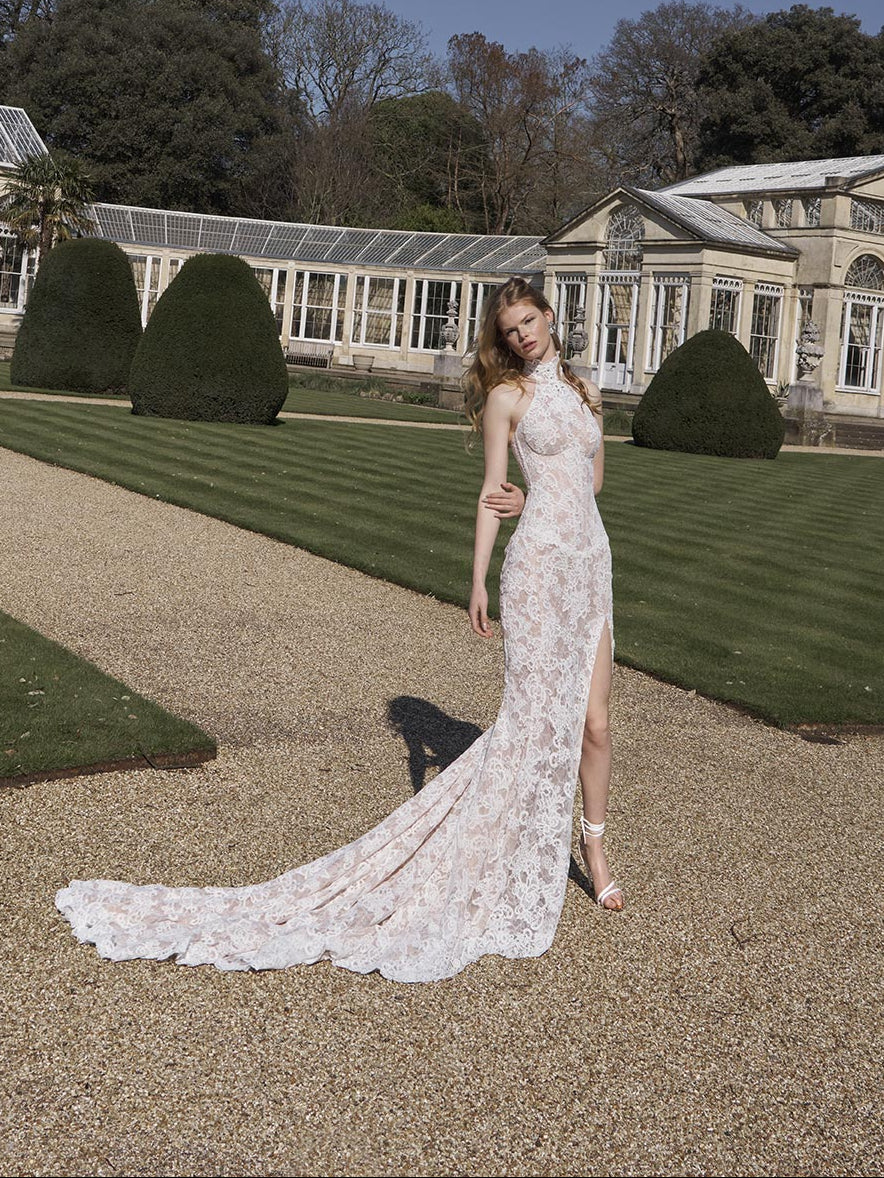 Woman in a white lace dress standing in a garden with a classical building in the background