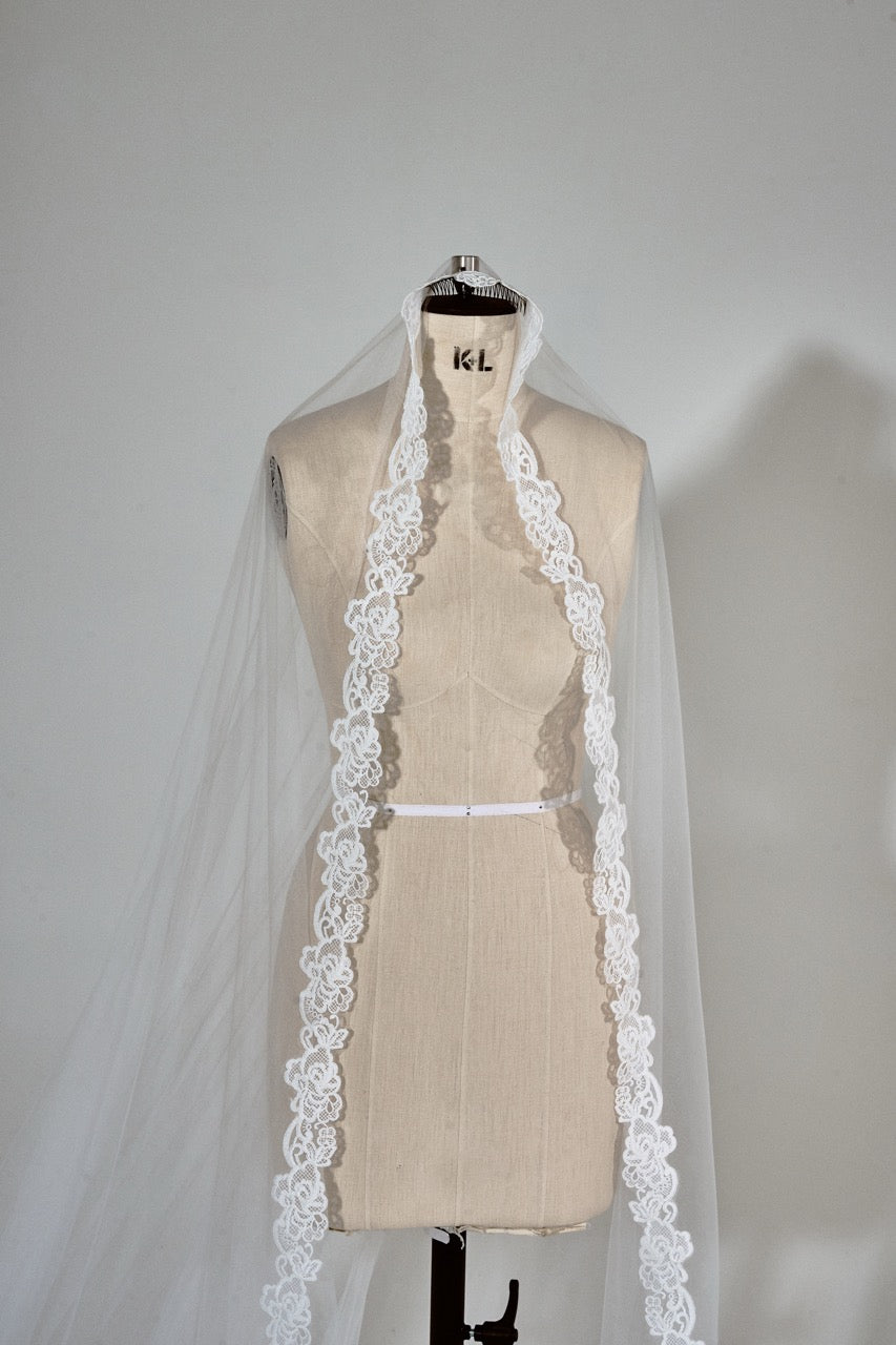 Beige dress with a white lace-trimmed veil on a mannequin against a plain background