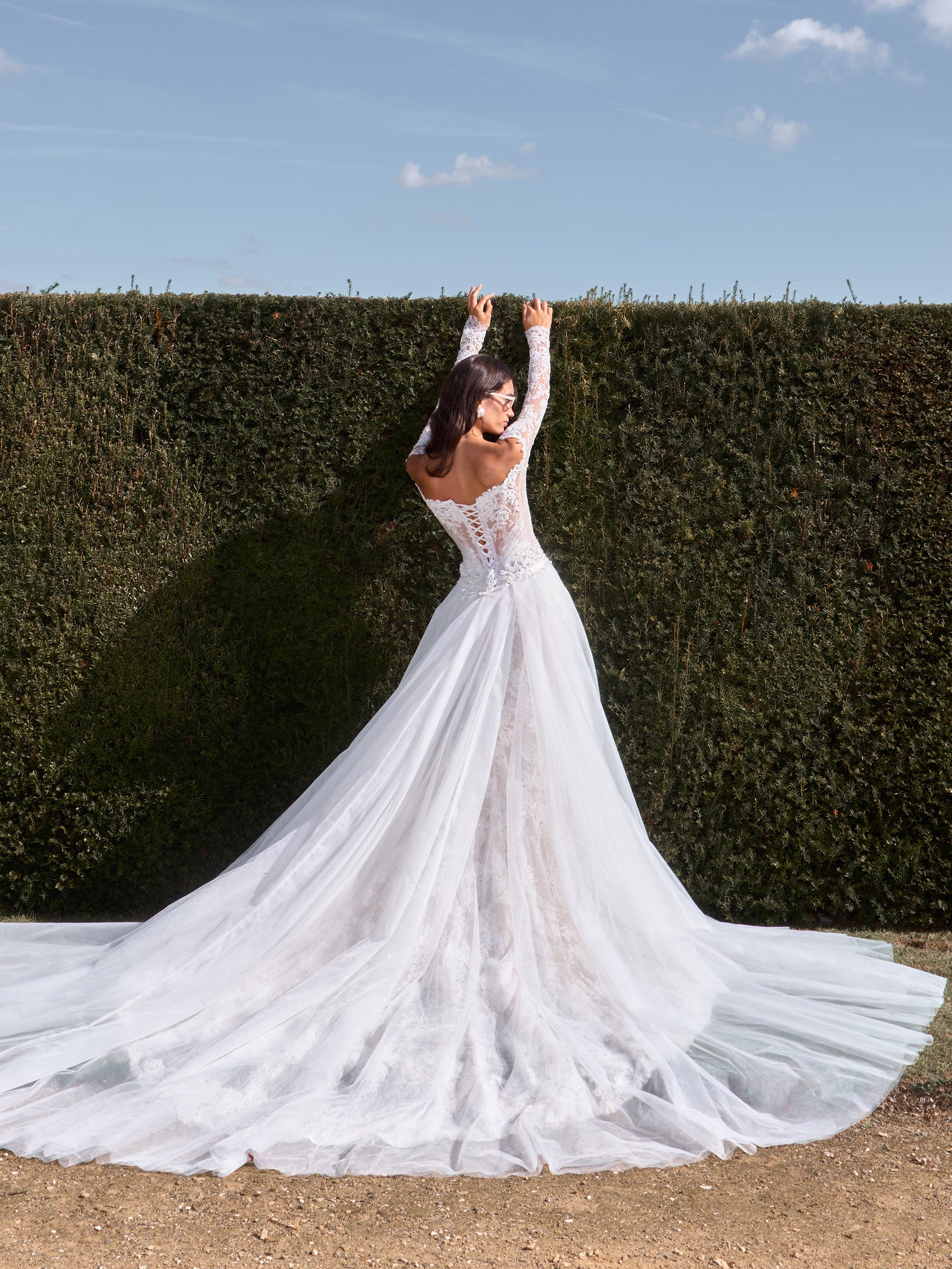 Woman in a white wedding dress standing in front of a hedge with a blue sky.