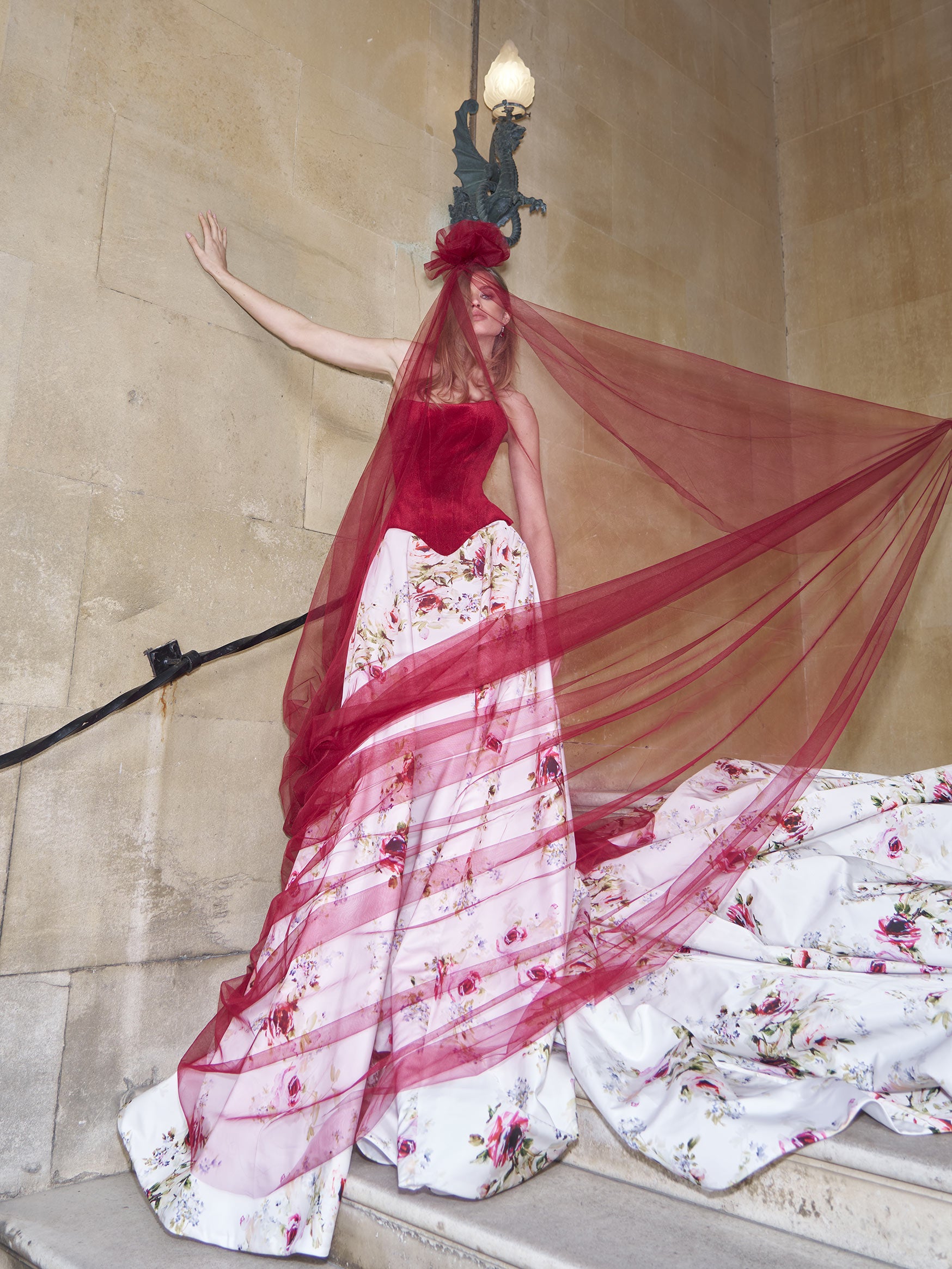 Woman in a red and white floral dress with a red veil standing on steps.