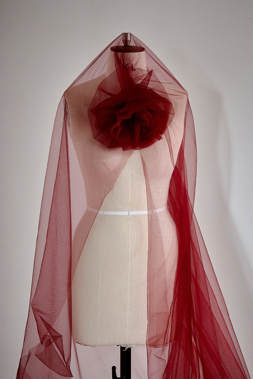 Red sheer fabric draped over a mannequin against a white background